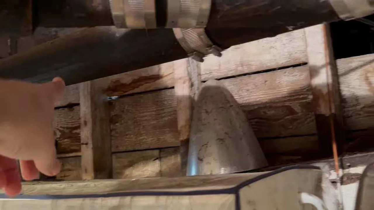 Old cast-iron drain pipe running beneath a wood floor